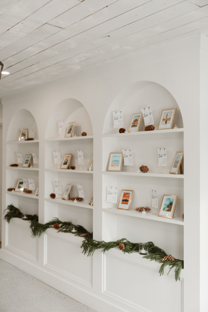 Grand Ivory wedding entrance with three arches and shelves displaying bride and groom’s photos, pinecones, and greenery