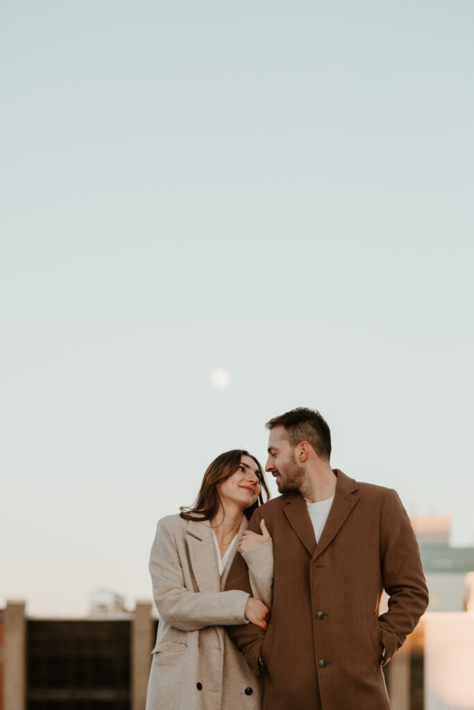 couple side by side gazing at each other outside engagement session with moon in background 