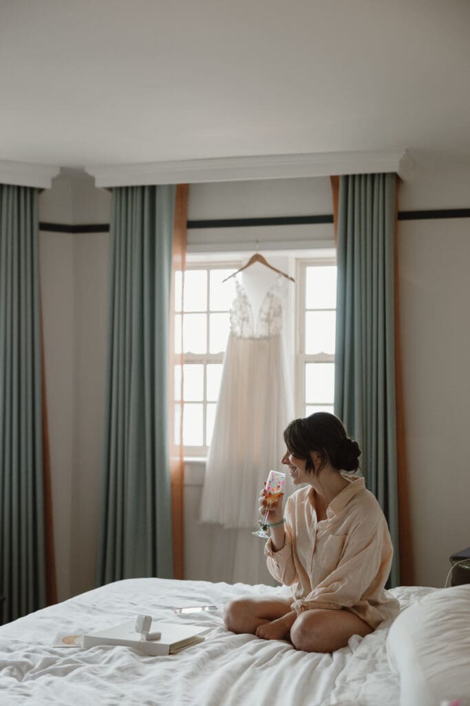Bride getting ready with dress hanging in background 
